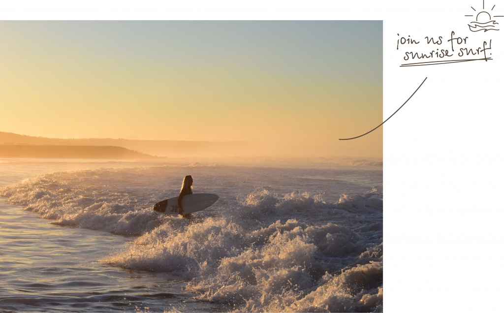 girl walking into the water holding a surfboard during sunrise