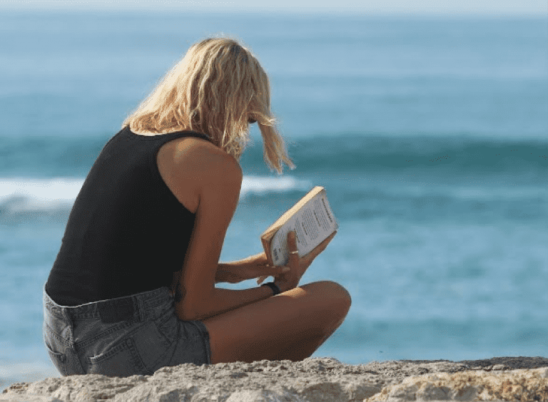 girl reading a book in front of the ocean