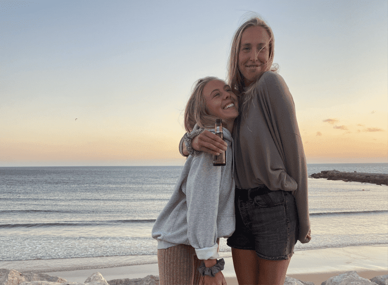 girls smiling and hugging in front of the ocean